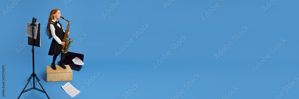 Naklejka premium Banner. Charming, talented young girl playing saxophone against blue studio background with negative space to insert text. Concept of children dreams, future career, occupation, games, fantasy. Ad