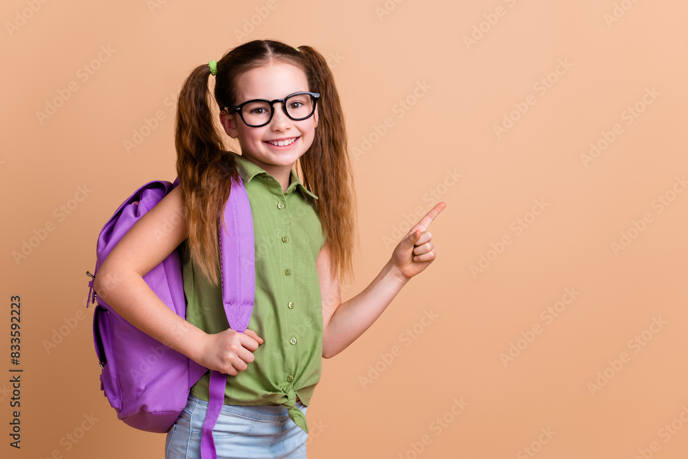 Photo of positive girl kid point finger copyspace hold rucksack isolated pastel color background