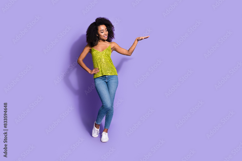 Full length photo of gorgeous young girl palm hold look empty space wear trendy green sequins outfit isolated on purple color background Full length photo of gorgeous young girl palm hold look empty space wear trendy green sequins outfit isolated on purple color background