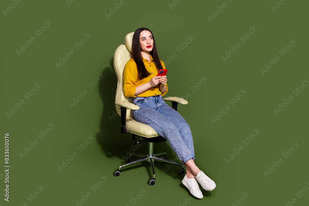 Full length photo of adorable lovely girl wear yellow shirt communicating modern gadget empty space isolated green color background Full length photo of adorable lovely girl wear yellow shirt communicating modern gadget empty space isolated green color background