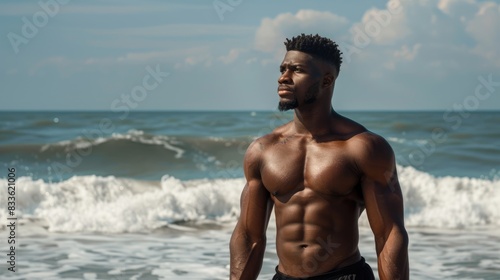 muscular black man standing on beach  looking out at ocean AIG51A.