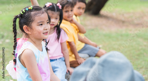 Group of multiracial children smiling  sitting at stone chair  playing together outdoors in summer park. Adorable kids have fun playing in playground. Selective focus on Asian girl