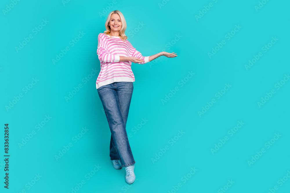 Full size photo of optimistic woman wear striped sweatshirt jeans palm presenting object empty space isolated on blue color background Full size photo of optimistic woman wear striped sweatshirt jeans palm presenting object empty space isolated on blue color background