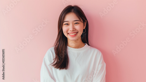Asian woman standing smiling, half body visible, white clothing with long sleeves Behind it is a light pink wall.