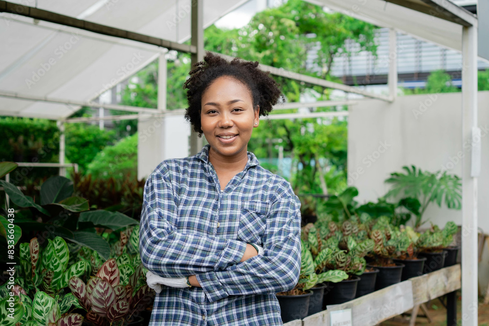 A woman in a plaid shirt stands in front of a greenhouse filled with plants. She is smiling and she is proud of her work A woman in a plaid shirt stands in front of a greenhouse filled with plants. She is smiling and she is proud of her work