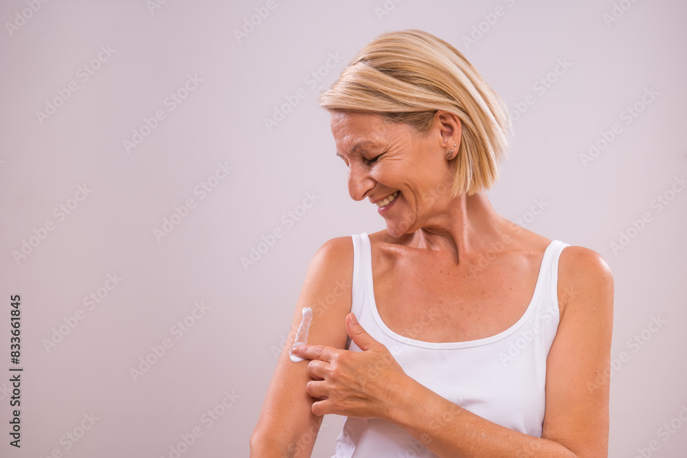 Portrait of beautiful mature woman applying moisturizer on her body. Portrait of beautiful mature woman applying moisturizer on her body.