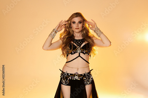 A captivating young woman in a stunning black and gold costume gracefully performs a mesmerizing belly dance. © LIGHTFIELD STUDIOS