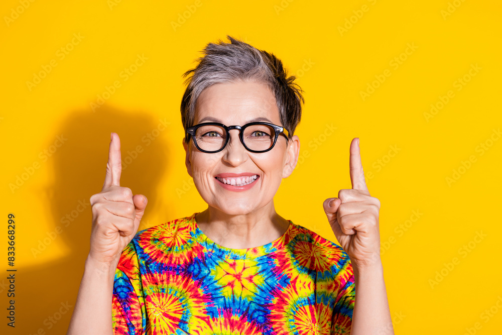 Photo of cheerful nice lovely retired woman wear trendy print clothes presenting empty space isolated on yellow color background Photo of cheerful nice lovely retired woman wear trendy print clothes presenting empty space isolated on yellow color background