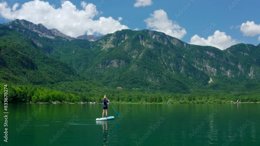 Aerial view of Person paddling on SUP board on Mountain Lake in Slovenia. Active Woman doing Water Sport on Bohinj alone. Stand up board as popular nature tourism relaxing leisure. 4K wide drone shot Aerial view of Person paddling on SUP board on Mountain Lake in Slovenia. Active Woman doing Water Sport on Bohinj alone. Stand up board as popular nature tourism relaxing leisure. 4K wide drone shot