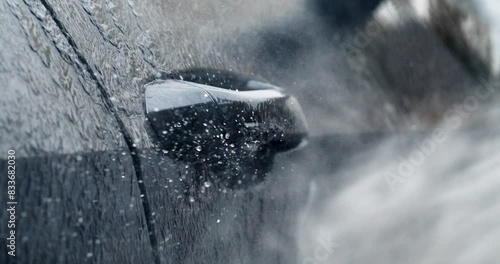 Super slow motion macro of modern auto vehicle detail under high pressure water jet during washing process on self service car wash. Manual car wash with pressurized water spray.