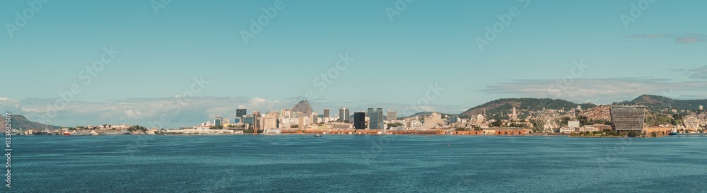 Fototapeta premium Panoramic view of Rio de Janeiro, Brazil, showcasing the city's skyline against a clear blue sky. The image features iconic buildings, lush hills, and the vast expanse of Guanabara Bay