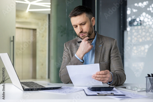 Fotografie A businessman deeply focused on analyzing documents at his desk in a modern office