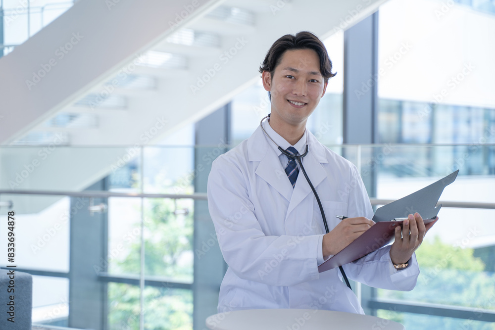 病院で笑顔でカルテに記入する男性医師