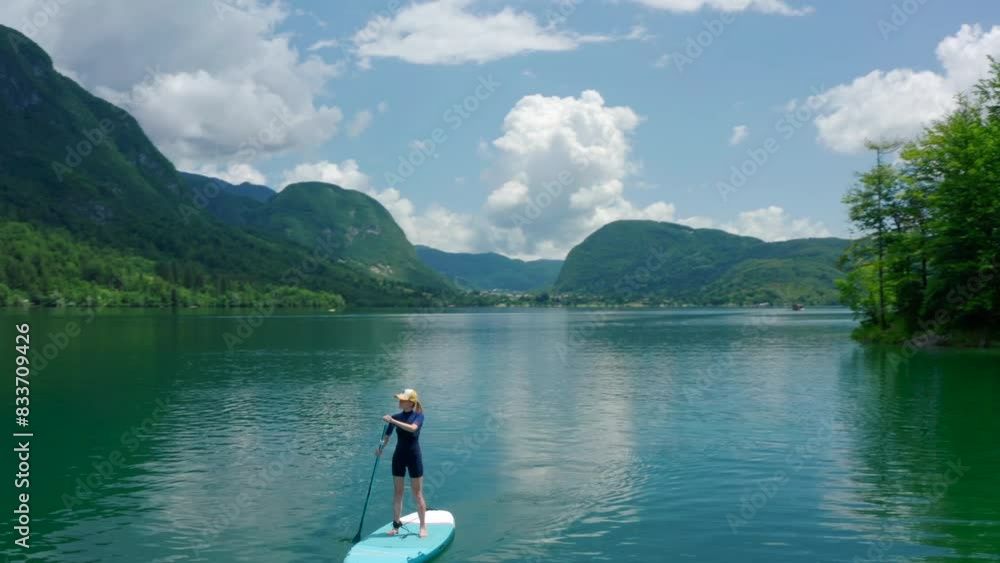 Aerial view of Fit Woman paddling fast on SUP board on Mountain Lake in Slovenia. Active Woman does Water Sport on Bohinj alone. Stand up board as popular nature tourism. 4K wide orbit drone shot Aerial view of Fit Woman paddling fast on SUP board on Mountain Lake in Slovenia. Active Woman does Water Sport on Bohinj alone. Stand up board as popular nature tourism. 4K wide orbit drone shot
