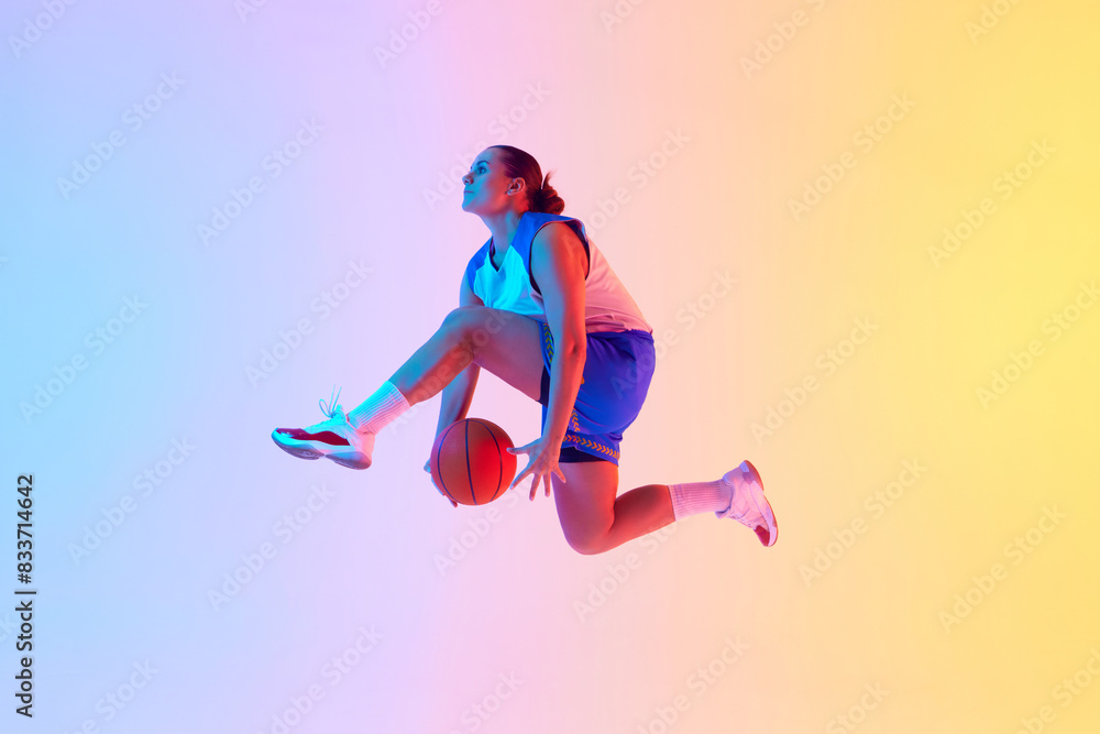 Dynamic photo of young basketball player leaping to make powerful slam dunk in neon light against gradient studio background. Concept of professional sport, championship, hobby and recreation. Ad
