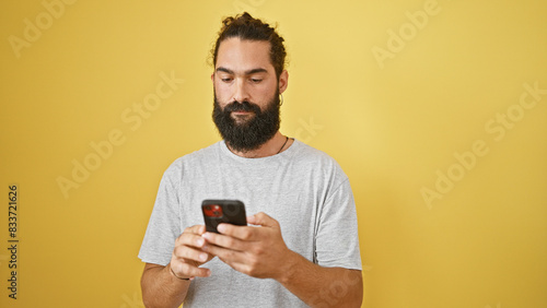 Hispanic man with beard using smartphone against yellow background
