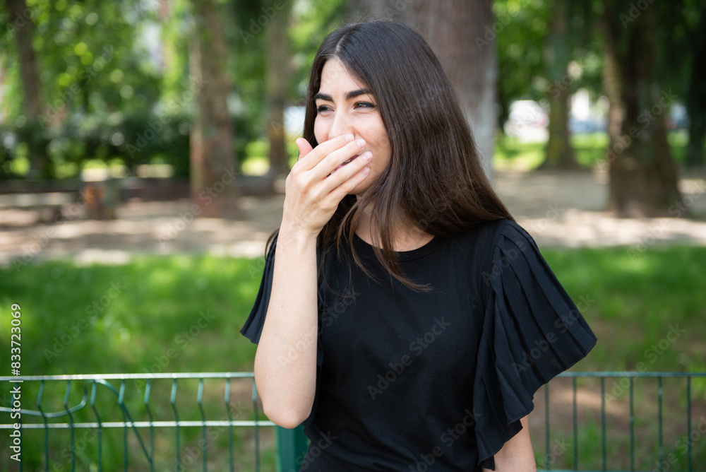 beautiful 30 years old woman laughing with a hand on her mouth in a park beautiful 30 years old woman laughing with a hand on her mouth in a park