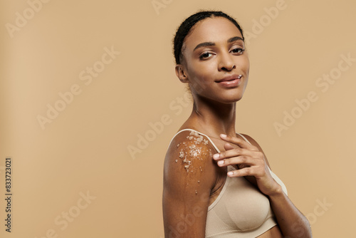 African American woman in underwear, gracefully adorned with scrub, on beige background.