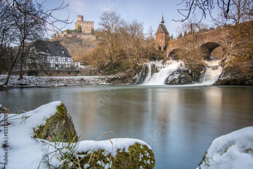 Beautiful landscape in winter with ice and snow. Waterfall of the River Elz near Pyrmont Castle, the Pyrmonter Mühle country inn is right on a lake. A historical bridge in Rhineland Pflaz, Germany photo