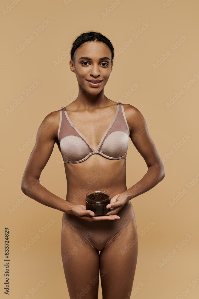 A slim African American woman in a bikini holding coffee scrub on a beige background. A slim African American woman in a bikini holding coffee scrub on a beige background.