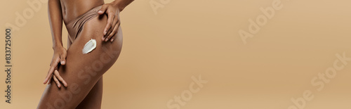 A gorgeous and slender African American woman wearing a bikini poses confidently on a beige background.