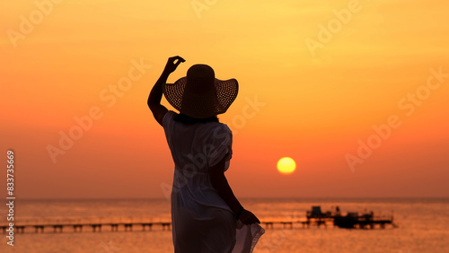 A strong, confident, beautiful woman under the rays of the setting sun on the ocean. Travel, femininity and relaxation concept.