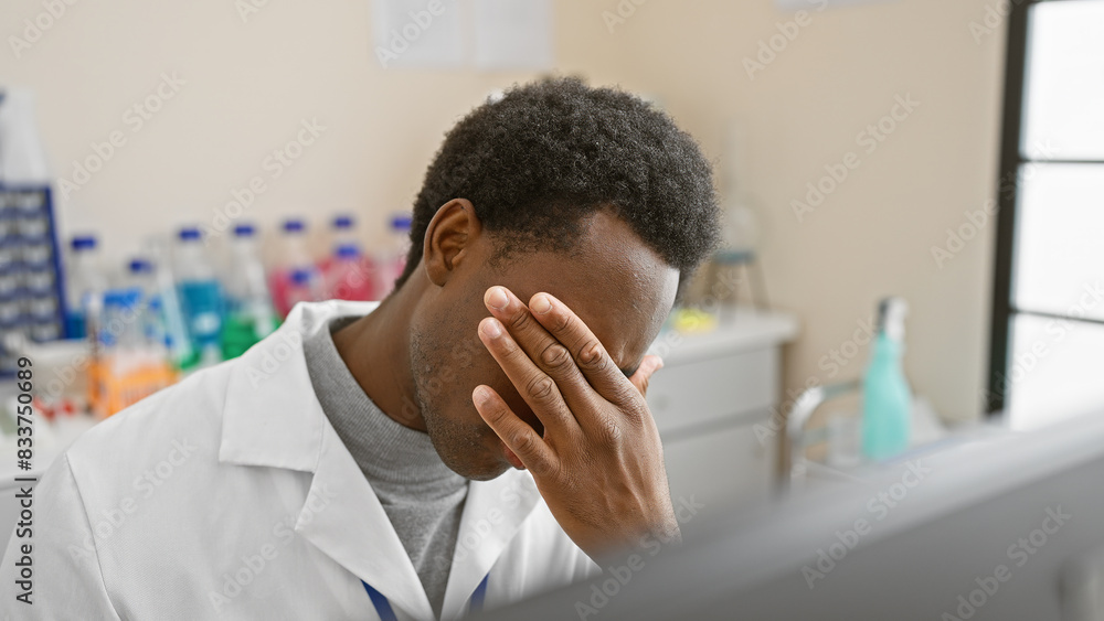 Tired african american man in a white lab coat resting head indoors at a medical laboratory. Tired african american man in a white lab coat resting head indoors at a medical laboratory.