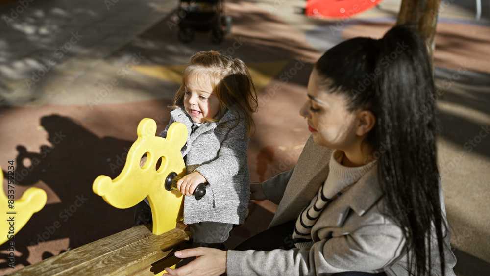 A smiling mother and daughter enjoying sunny day at an outdoor playground, bonding over a seesaw ride. A smiling mother and daughter enjoying sunny day at an outdoor playground, bonding over a seesaw ride.