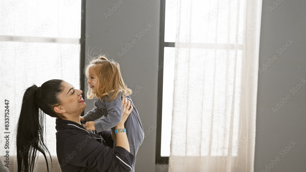 A smiling woman holds her joyful daughter in a bright bedroom, depicting family, happiness, and home comfort. A smiling woman holds her joyful daughter in a bright bedroom, depicting family, happiness, and home comfort.