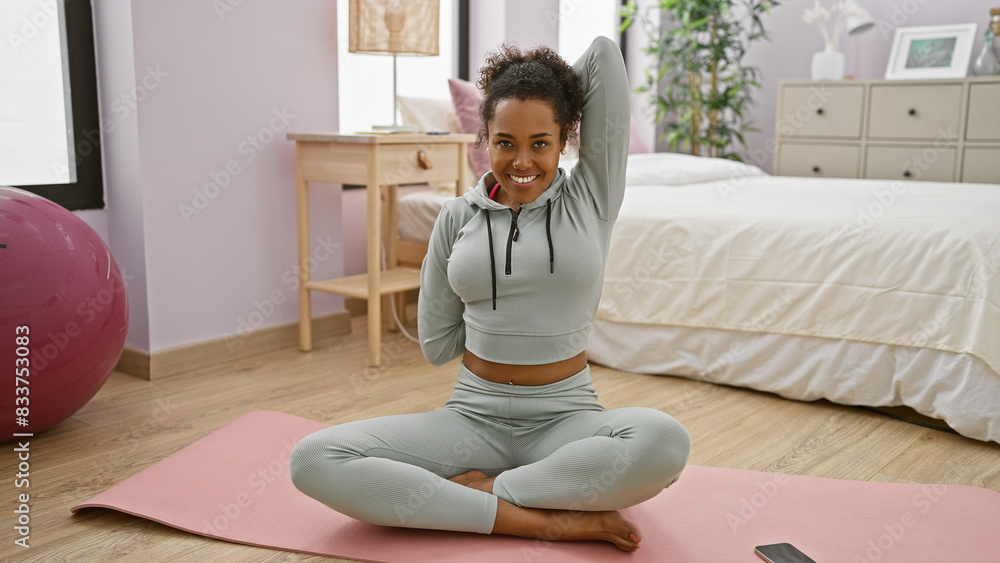 An athletic woman with curly hair stretches on a yoga mat in her contemporary bedroom. An athletic woman with curly hair stretches on a yoga mat in her contemporary bedroom.