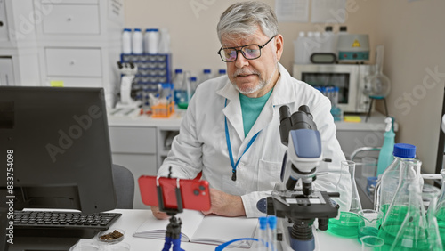 Middle-aged man conducting a video call in a laboratory setting with scientific equipment around him.
