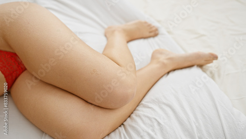 Close-up of a young woman's legs on a white bed in an indoor bedroom setting.