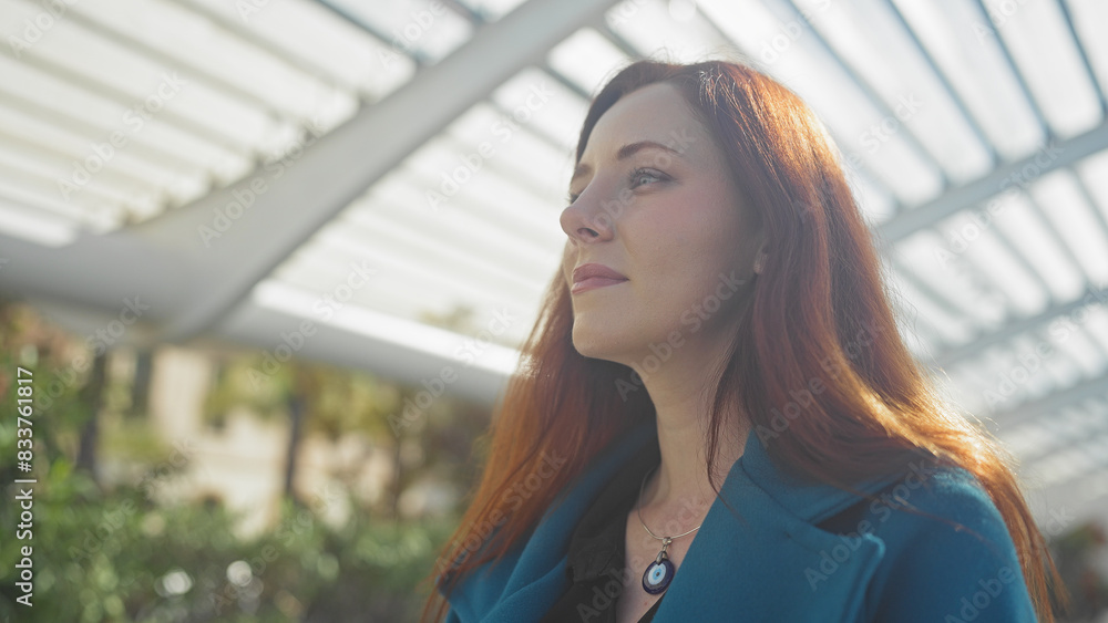 A beautiful young adult redhead woman in thoughtful pose, outdoor in an urban park with a modern structure A beautiful young adult redhead woman in thoughtful pose, outdoor in an urban park with a modern structure