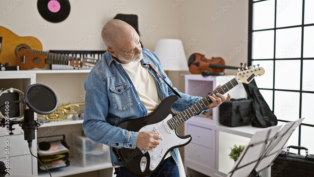 Fototapeta premium A middle-aged man plays an electric guitar in a home music studio with instruments in the background.