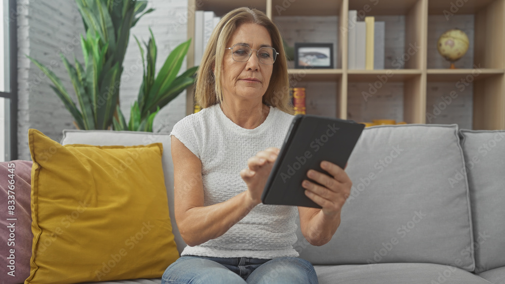 Mature woman reading tablet on sofa in a cozy living room Mature woman reading tablet on sofa in a cozy living room