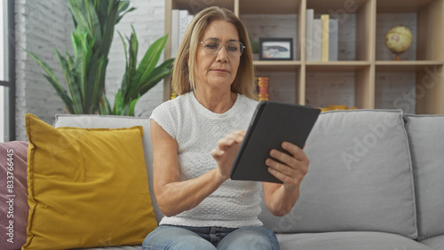 Mature woman reading tablet on sofa in a cozy living room