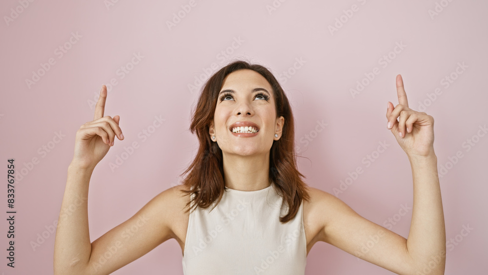 Smiling young woman with hispanic features pointing upwards against a pink background, portraying positivity. Smiling young woman with hispanic features pointing upwards against a pink background, portraying positivity.