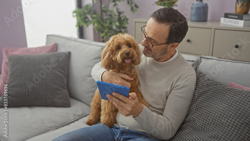 Hispanic man enjoys leisure time with poodle while using tablet in cozy living room
