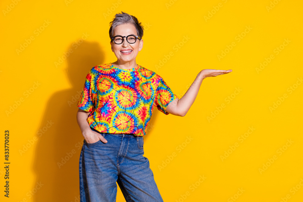 Photo of lovely pretty senior woman wear trendy clothes hold empty space isolated on yellow color background Photo of lovely pretty senior woman wear trendy clothes hold empty space isolated on yellow color background