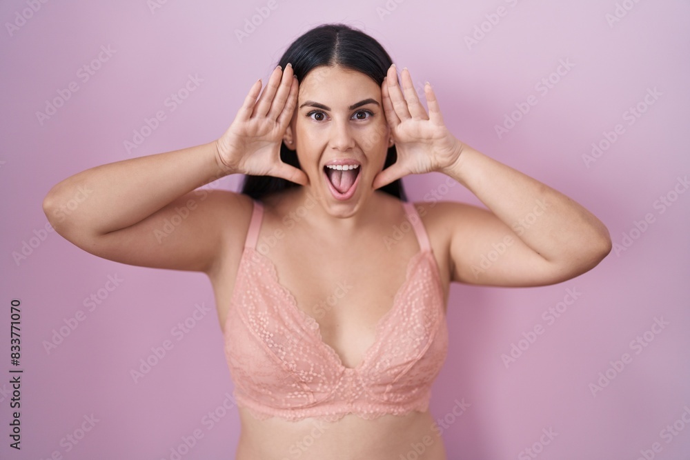 Young hispanic woman wearing pink bra smiling cheerful playing peek a boo with hands showing face. surprised and exited Young hispanic woman wearing pink bra smiling cheerful playing peek a boo with hands showing face. surprised and exited