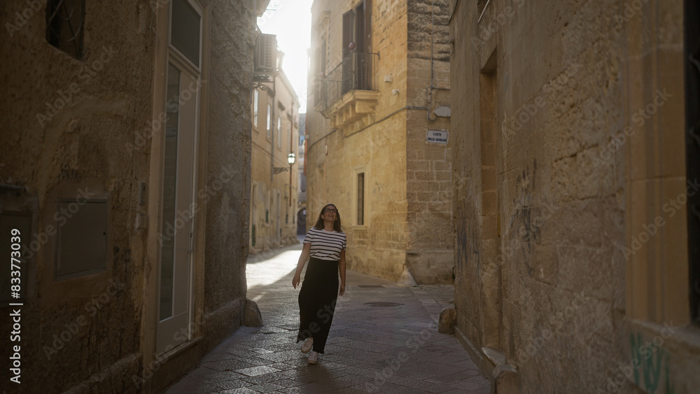 A beautiful young hispanic woman walks through a narrow town alley in lecce, puglia, italy, enjoying the sunny day.