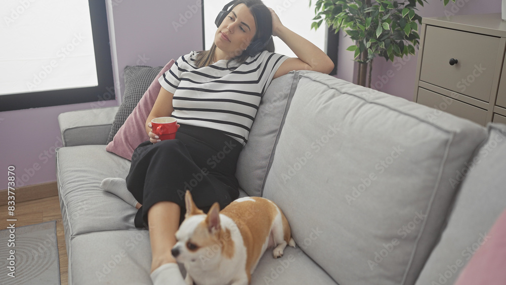A woman relaxes on a sofa with headphones, a coffee cup, and a chihuahua in a cozy living room. A woman relaxes on a sofa with headphones, a coffee cup, and a chihuahua in a cozy living room.