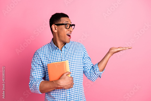 Photo of attractive excited guy wear plaid shirt enjoying book holding arm emtpy space isolated pink color background photo