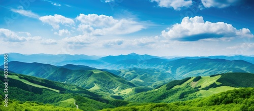 Stunning nature scenery with a beautiful blue sky, fluffy white clouds, and lush green hills. Perfect as a nature background or wallpaper, taken from the mountain peak, ideal for a copy space image.