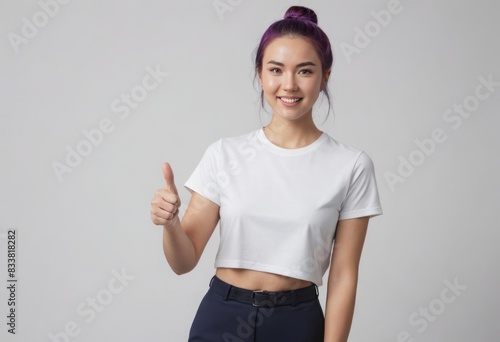 A young woman in a cropped white t-shirt gives a thumbs up, her casual look and upbeat attitude radiating positivity.