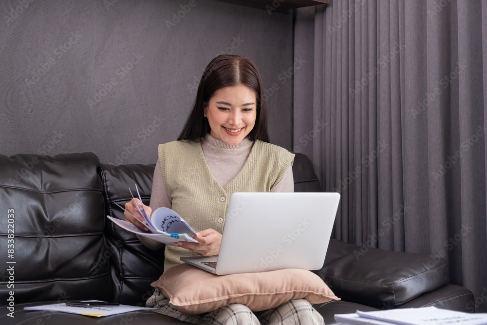 Woman Using Laptop and Reading Document on Sofa. Concept of multitasking and modern work lifestyle. Woman Using Laptop and Reading Document on Sofa. Concept of multitasking and modern work lifestyle.