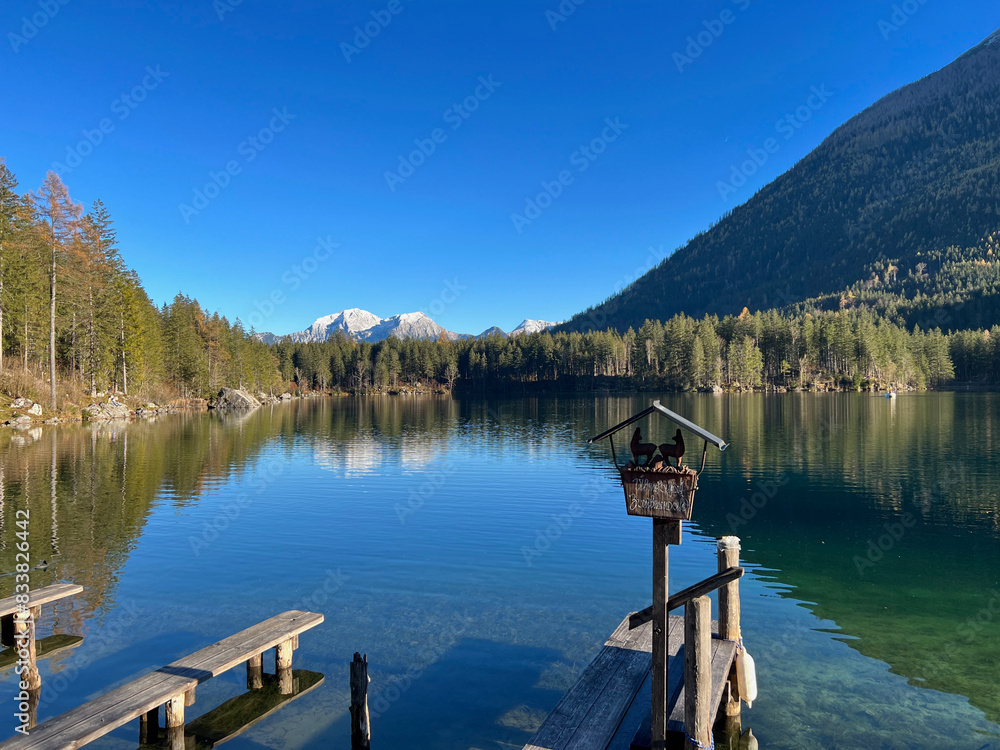 Small wooden pier on the clear waters of Lake Hintersee in Bavaria, Germany, with forested shoreline and mountain backdrop. Small wooden pier on the clear waters of Lake Hintersee in Bavaria, Germany, with forested shoreline and mountain backdrop.