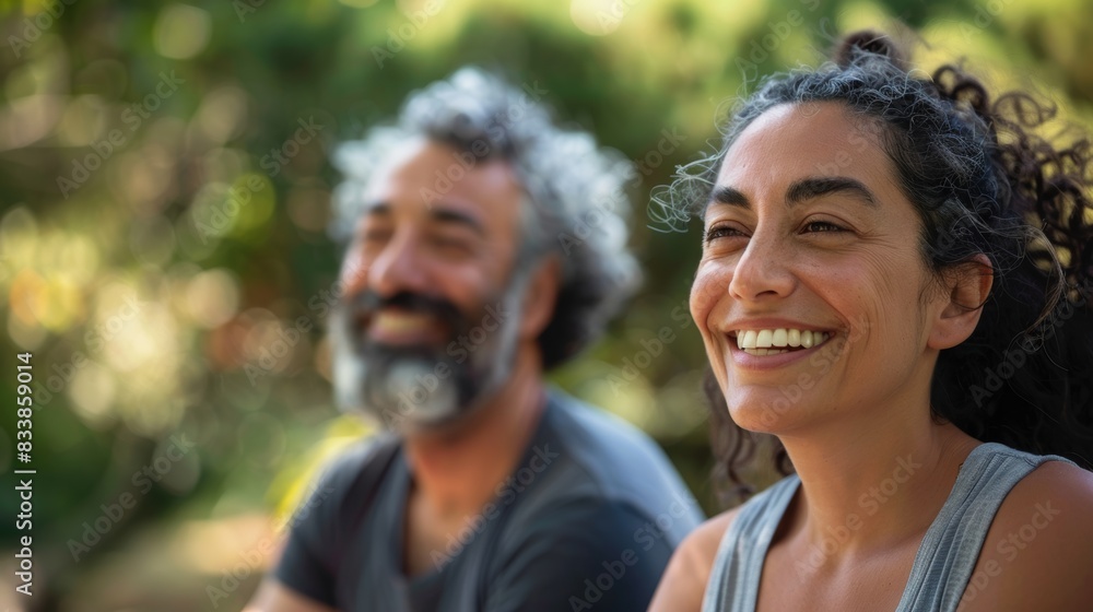 A man and woman sitting together smiling and enjoying each other's company in a natural setting with blurred greenery in the background. A man and woman sitting together smiling and enjoying each other's company in a natural setting with blurred greenery in the background.