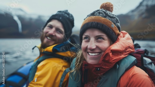 Two smiling hikers in winter gear enjoying a moment of adventure on a mountain lake.