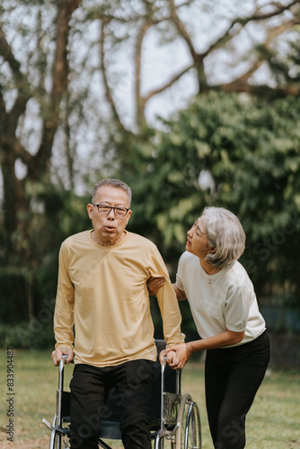 Elderly Asian couple and wife caring for their family enjoying retirement together in park. Old Caregiver people take close care while using walking cane stick © Wicitr